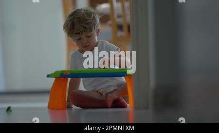 Un enfant assis au sol joue avec un plan magnétique effaçable à la maison. scène de style de vie enfant Banque D'Images
