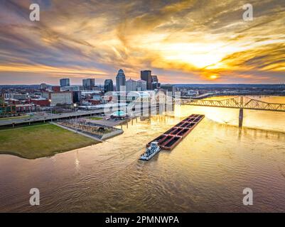 Un lever de soleil majestueux projette ses rayons sur un paysage urbain animé, tandis qu'une grande barge navigue le long des eaux tranquilles Banque D'Images