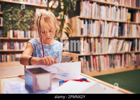 Écolière faisant ses devoirs. Apprentissage des élèves du primaire, dessin de photos, faire des puzzles au bureau dans la bibliothèque scolaire. Étudiant primaire dans le club scolaire Banque D'Images