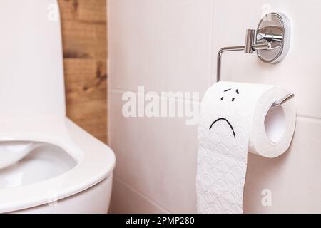 gros plan sur une émoticône triste sur un rouleau de papier toilette suspendu dans la salle de toilettes Banque D'Images