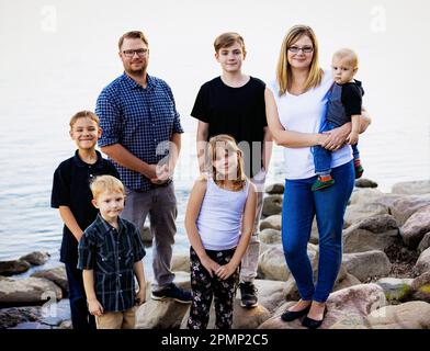 Portrait extérieur d'une famille avec cinq jeunes enfants debout sur des rochers au bord d'un lac tranquille; Edmonton, Alberta, Canada Banque D'Images