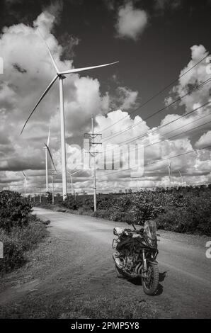 Une grosse moto noire garée sur une piste de terre à côté d'une ligne de transmission de puissance, d'énormes éoliennes et une plantation de café dans la province de Gia Lai Banque D'Images