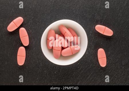 Plusieurs pilules médicales en soucoupe céramique blanche sur pierre d'ardoise, macro, vue de dessus. Banque D'Images