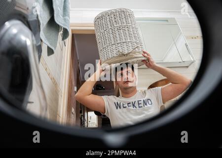 Homme avec panier sur la tête, vue depuis le lave-linge à l'intérieur. Un homme fait la lessive tous les jours. Banque D'Images