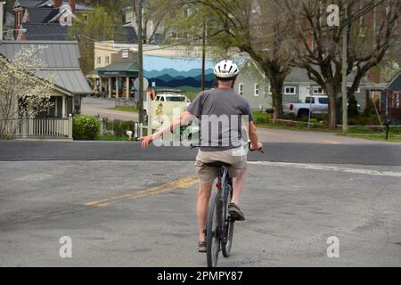 Un homme de haut niveau qui fait du vélo signale un virage à gauche lorsqu'il se déplace le long d'une rue à Abingdon, en Virginie. Banque D'Images