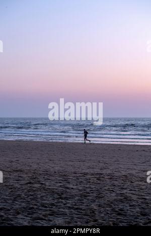 Homme marchant le long d'une plage au coucher du soleil à Cornwall, Angleterre, Royaume-Uni Banque D'Images