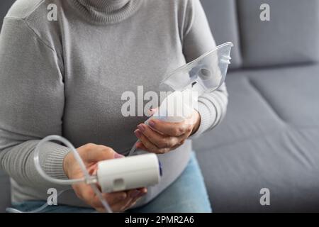 Femme âgée utilisant un nébuliseur fait l'inhalation à la maison et regarde la caméra Banque D'Images