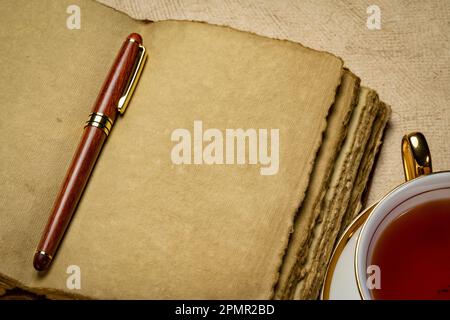 journal en cuir rétro vierge avec feuilles de papier à la main à bords décalés, stylo élégant et concept de journalisation pour une tasse de thé Banque D'Images