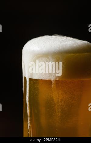 Bière froide avec mousse dans une tasse un fond sombre, gros plan. Banque D'Images