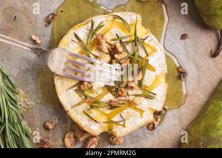 Délicieux camembert au four avec fourchette. Fromage au miel, noix, herbes et poires Banque D'Images