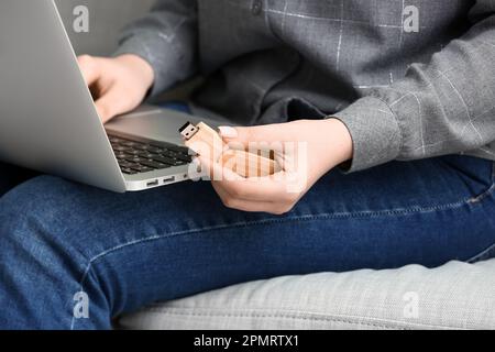 Femme avec ordinateur portable moderne et lecteur flash USB en bois assis sur un canapé, gros plan Banque D'Images