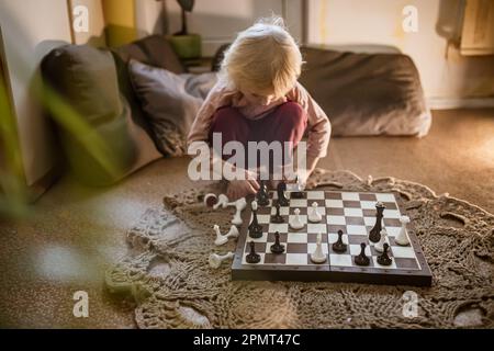 l'enfant joue une seule partie d'échecs à la maison sur le sol.Échiquier avec la fin de la partie d'échecs.La main de la fille se déplaçant une pièce d'échecs est partiellement visible Banque D'Images