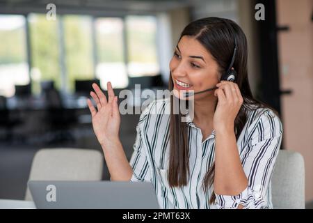 Brunette Lady appel vidéo sur ordinateur portable port casque souriant et passant la main à la webcam communiquant en ligne Banque D'Images