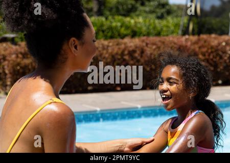 Bonne mère et fille biraciale se tenant les mains près de la piscine dans le jardin ensoleillé Banque D'Images