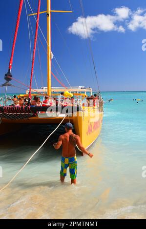 Un ouvrier aide à guider un catamaran plein de touristes et de voyageurs, après leur journée sur l'océan et sur les sables de Waikiki Beach à Hawaï Banque D'Images