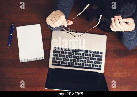 Vue de dessus d'une femme d'affaires tenant des lunettes pendant qu'elle travaille sur un ordinateur portable Banque D'Images