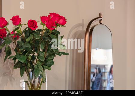 Roses rouges dans un vase en verre transparent sur la table près du miroir. Banque D'Images