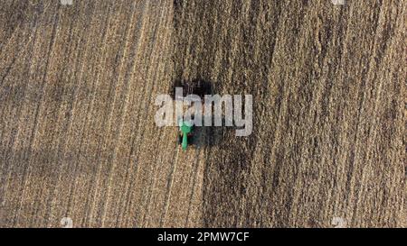 Le tracteur labourage le sol. En survolant un tracteur vert qui plâche le sol dans un champ jaune après avoir récolté du blé le jour de l'automne. Travaux agricoles sur le terrain. Terrain de creusement du tracteur. Vue aérienne de drone Banque D'Images