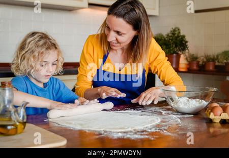 Cuisine familiale: Bonne mère et fils ayant plaisir à préparer la pizza de pâte à l'intérieur de la cuisine maison - attention douce sur le visage de maman Banque D'Images