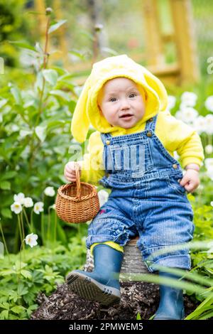 enfant en costume aux jardiniers et bottes en caoutchouc s'assoit sur une souche avec un panier. Concept d'usine de plantation Banque D'Images