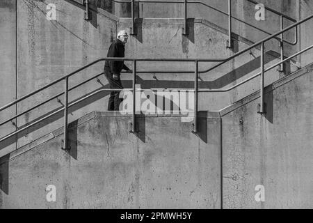 un homme âgé monte un escalier en béton avec une main courante Banque D'Images