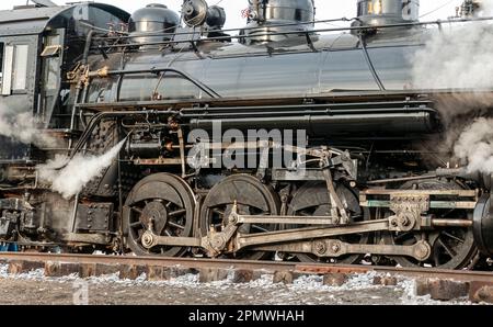 Un gros plan d'un train à vapeur entraîne un train d'engrenages lorsqu'il passe avec la vapeur qui s'échappe Banque D'Images