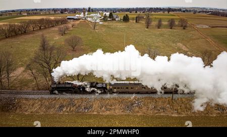 Ronks, Pennsylvanie, 27 décembre 2022 - Vue aérienne latérale d'un train de passagers à vapeur qui s'approche, traversant des terres agricoles ouvertes, soufflant beaucoup de fumée blanche, le jour d'hiver Banque D'Images