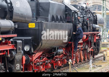 Dresde, Allemagne. 15th avril 2023. Un homme monte à bord de la locomotive 528154-8, qui est garée sur une voie à l'extérieur de l'édifice de la gare, et est surveillé par un autre homme. Les fans de chemin de fer avec des trains historiques se réunissent pour la réunion des locomotives à vapeur de Dresde en 15th à l'occasion du 125th anniversaire de la gare centrale de Dresde. Credit: Daniel Schäfer/dpa/Alay Live News Banque D'Images