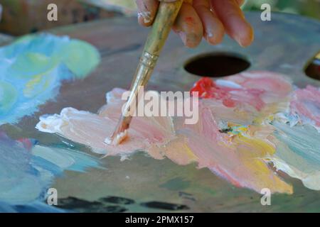 Photo des doigts mélangeant des peintures sur une palette avec un pinceau Banque D'Images
