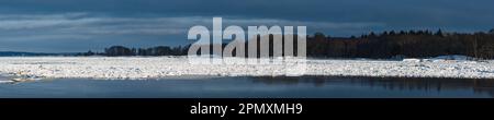 La beauté de l'hiver en Suède se révèle dans la rivière glacée reflétant un ciel sombre et sinistre, encadré par un paysage gelé. Banque D'Images