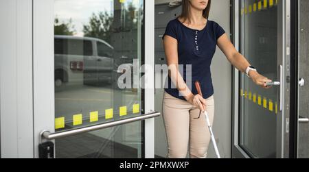 Une jeune femme malvoyante marchant dans les rues de la ville, utilisant sa canne blanche pour mieux naviguer dans l'espace urbain et pour se rendre à destination en toute sécurité Banque D'Images
