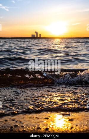 Coucher de soleil sur le lac Störmthal. les vagues sont comme du verre sur la plage. le soleil se réfléchit sur l'eau. Loin en arrière-plan, la centrale électrique de Lippendorf. Banque D'Images