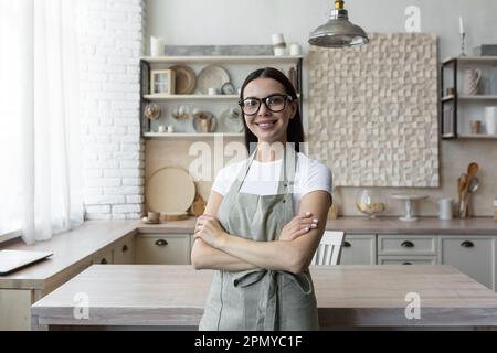 Portrait d'une jeune blogueuse debout à la maison dans la cuisine dans un tablier et regardant la caméra. Blogs sur l'économie domestique et la cuisine. Banque D'Images
