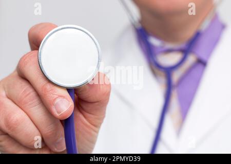 Médecin méconnaissable tenant un stéthoscope mettant la cloche vers la caméra. Gros plan de l'instrument avec mise au point sélective et arrière-plan flou Banque D'Images