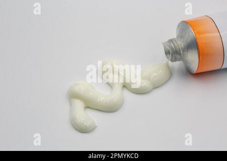 Ligne de crème blanche composée en quiggly étant comprimée hors d'un tube de pommade de pharmacie d'ordonnance sur un fond blanc de gros plan. Banque D'Images