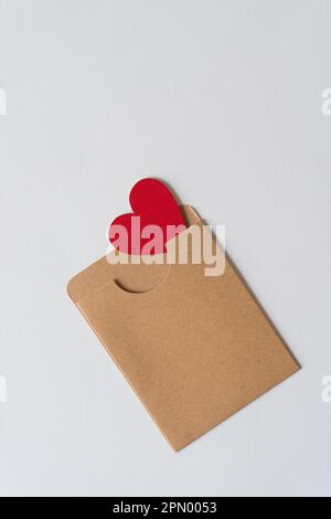 ornement coeur rouge caché en partie dans une enveloppe de poche en papier marron Banque D'Images