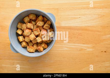 Croûtons d'herbes fraîches et d'ail faits de pain français de jour dans un bol en plastique bleu. Sur fond de bloc de boucherie en bois en composition de couche plate Banque D'Images