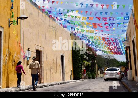 Les touristes se promenant dans une rue bordée de papel picado à Izamal, Yucatan, Mexique. Banque D'Images