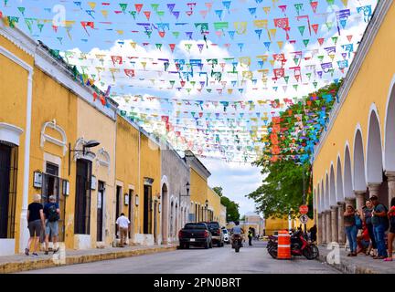 Une rue colorée avec des gens et des véhicules et papel picado (papier perforé) dans la ville jaune d'Izamal, Yucatan, Mexique. Banque D'Images