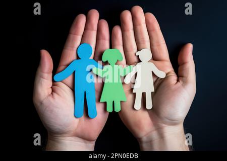 Personne anonyme qui fait la démonstration de mains avec une famille colorée coupée du papier sur fond noir Banque D'Images