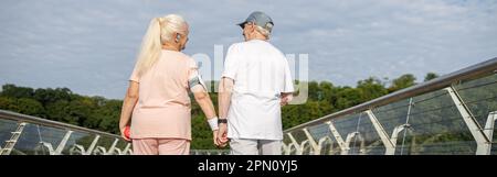 Une femme et un homme âgés positifs marchent en tenant les mains le long de la passerelle après l'entraînement Banque D'Images