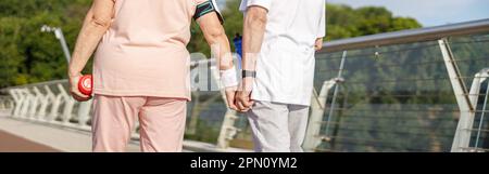 Un couple senior en survêtements se joindra aux mains le long de la passerelle au coucher du soleil Banque D'Images