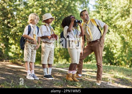 Vue latérale à divers groupes de scouts dans la forêt explorant la nature avec petite fille regardant dans des jumelles Banque D'Images