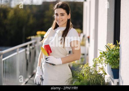 Jeune femme attrayante dans l'ensemble avec les outils de jardin se tiennent sur le balcon et se préparant à l'atterrissage Banque D'Images