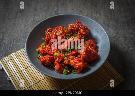 Yangnyeom Tongdak (poulet frit épicé coréen) ailes de poulet épicées en sauce aigre-douce sur fond rustique Banque D'Images