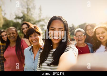 Heureux groupe multigénérationnel de femmes avec différentes origines ethniques s'amusant prendre selfie avec appareil photo de smartphone dans un parc public Banque D'Images