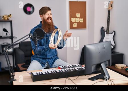 Jeune redhead homme musicien chant chanson jouant tambourine dans un studio de musique Banque D'Images