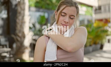 Jeune femme blonde portant des vêtements de sport massant le dos pour les blessures dans la rue Banque D'Images