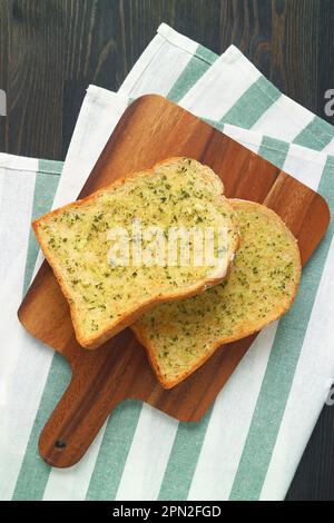 Paire de toasts au beurre d'ail sur une plaque en bois sur une table en bois noir Banque D'Images