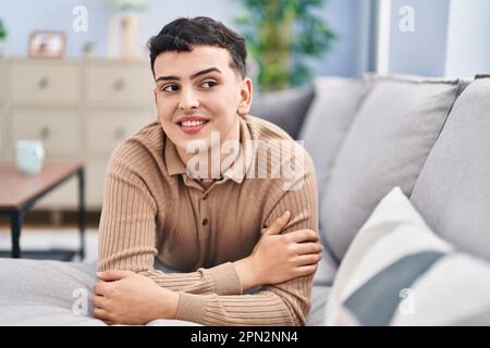 Jeune homme non binaire souriant confiant allongé sur un canapé à la maison Banque D'Images
